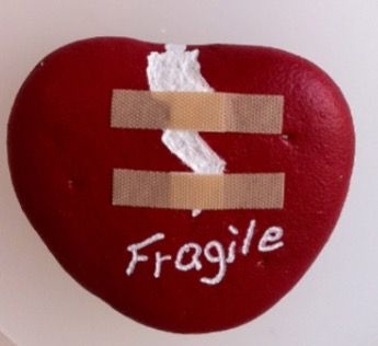 Cuore rosso incrinato, tenuto insieme da due cerotti, con la scritta Fragile