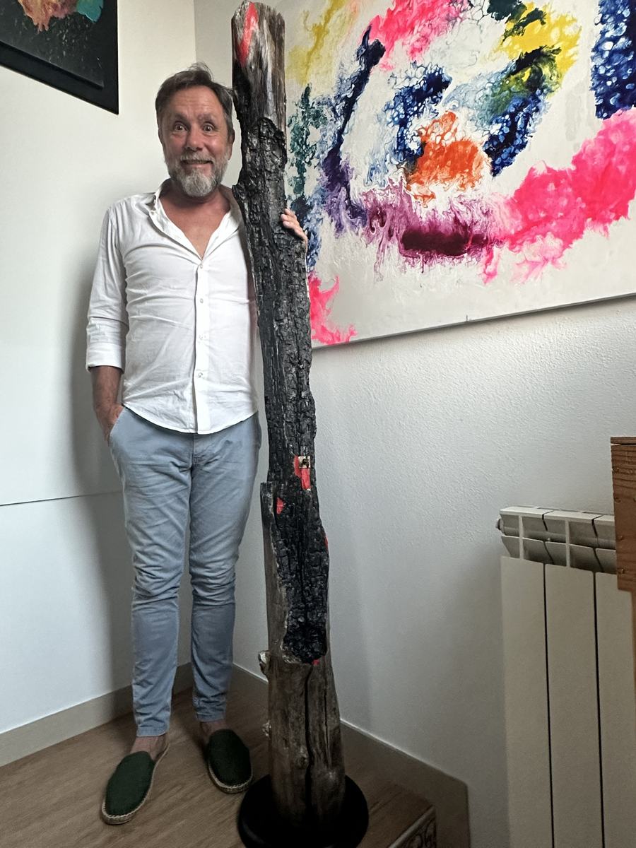 Stefano accanto a un tronco bruciato alto quanto lui, con macchie di rosso